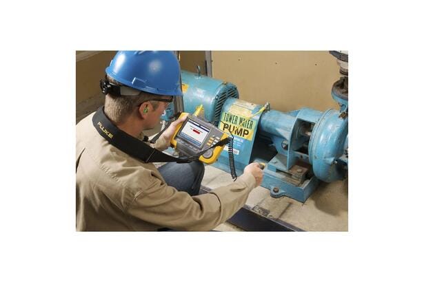 Mand med hjelm benytter Fluke 810 vibrationsanalysator til måling på en industripumpe.